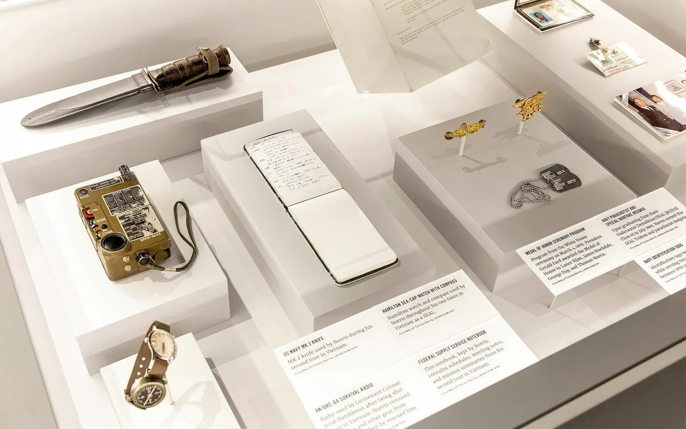 Personal artifacts in a display case: a knife, a radio, a pocket notebook, a watch and insignia