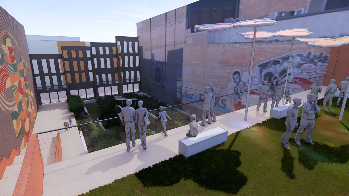 People gather on a lawn terrace with benches, looking down over a garden toward brick buildings and murals