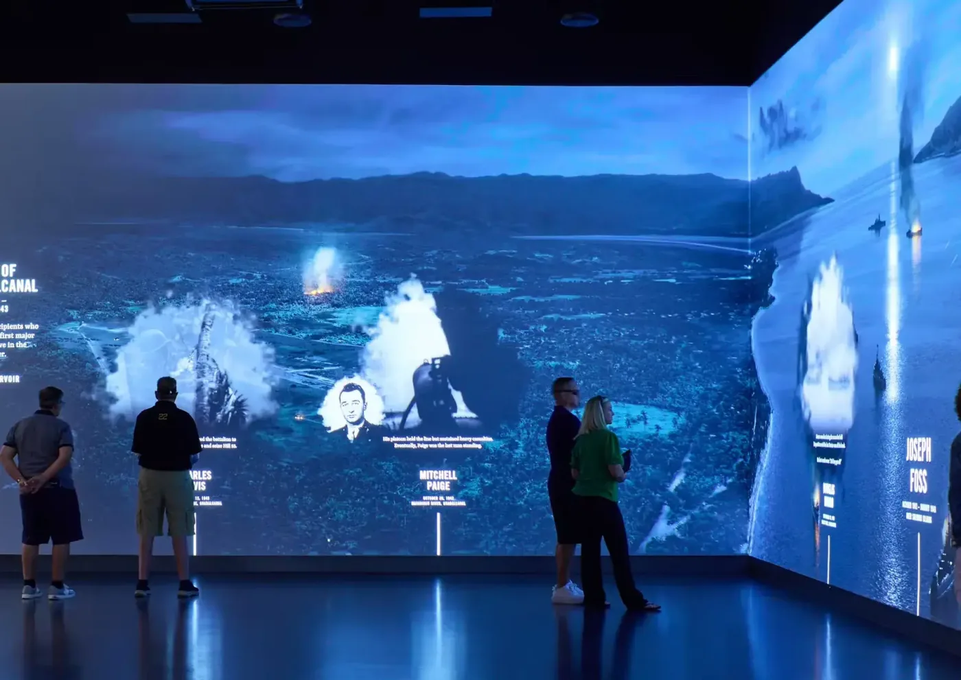 Visitors stand before a wraparound projection of a nighttime sea battle