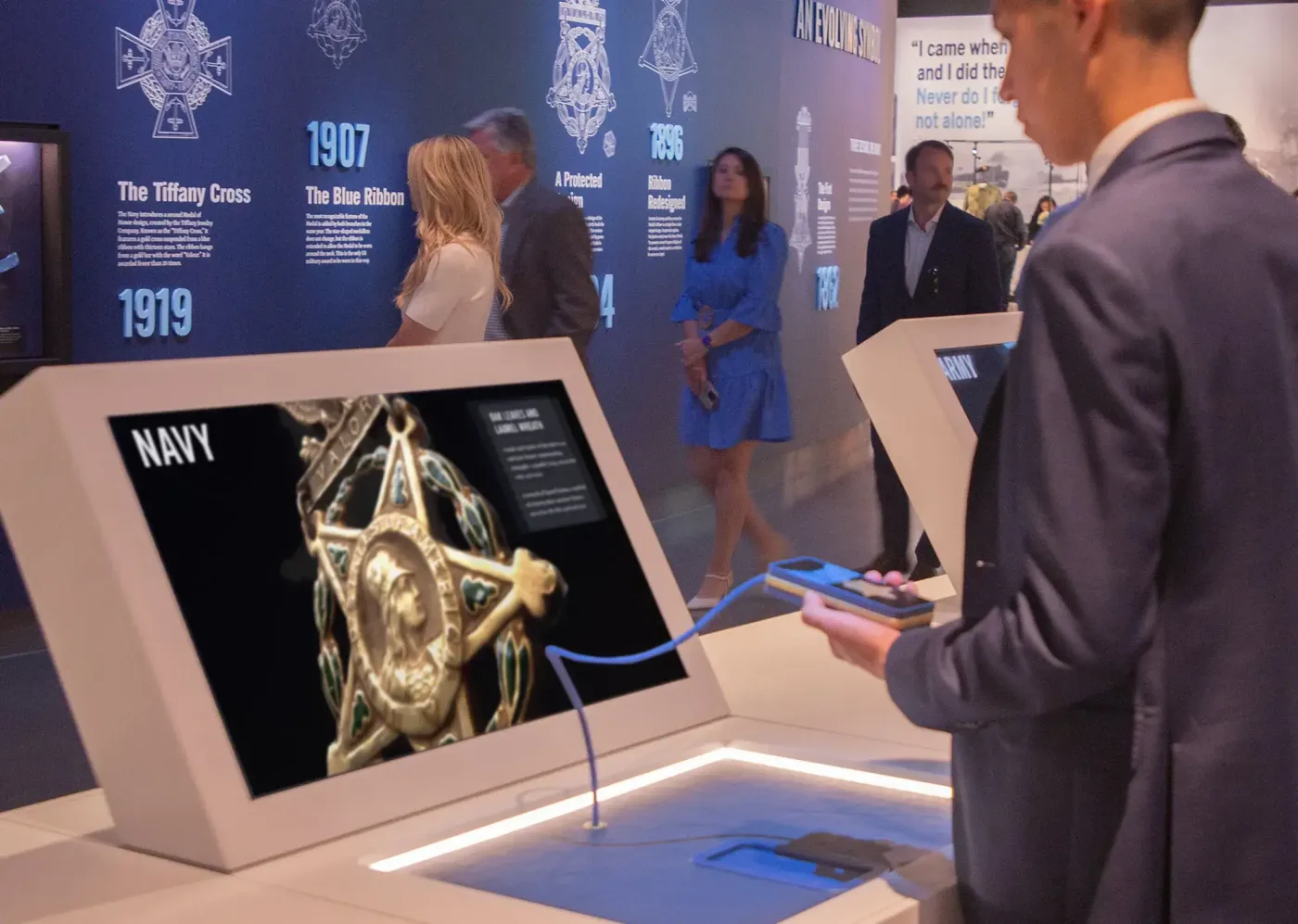Visitors at an interactive table showing the Navy Medal of Honor, with a timeline of medal designs behind