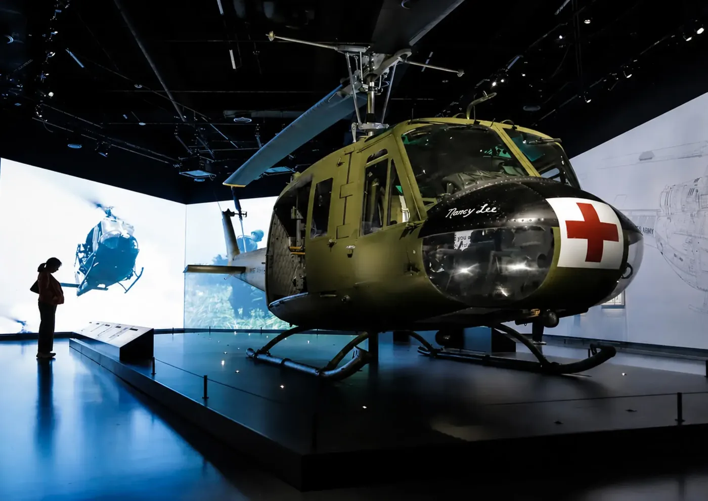 A Vietnam-era medical evacuation helicopter displayed in a gallery, a visitor silhouetted beside it